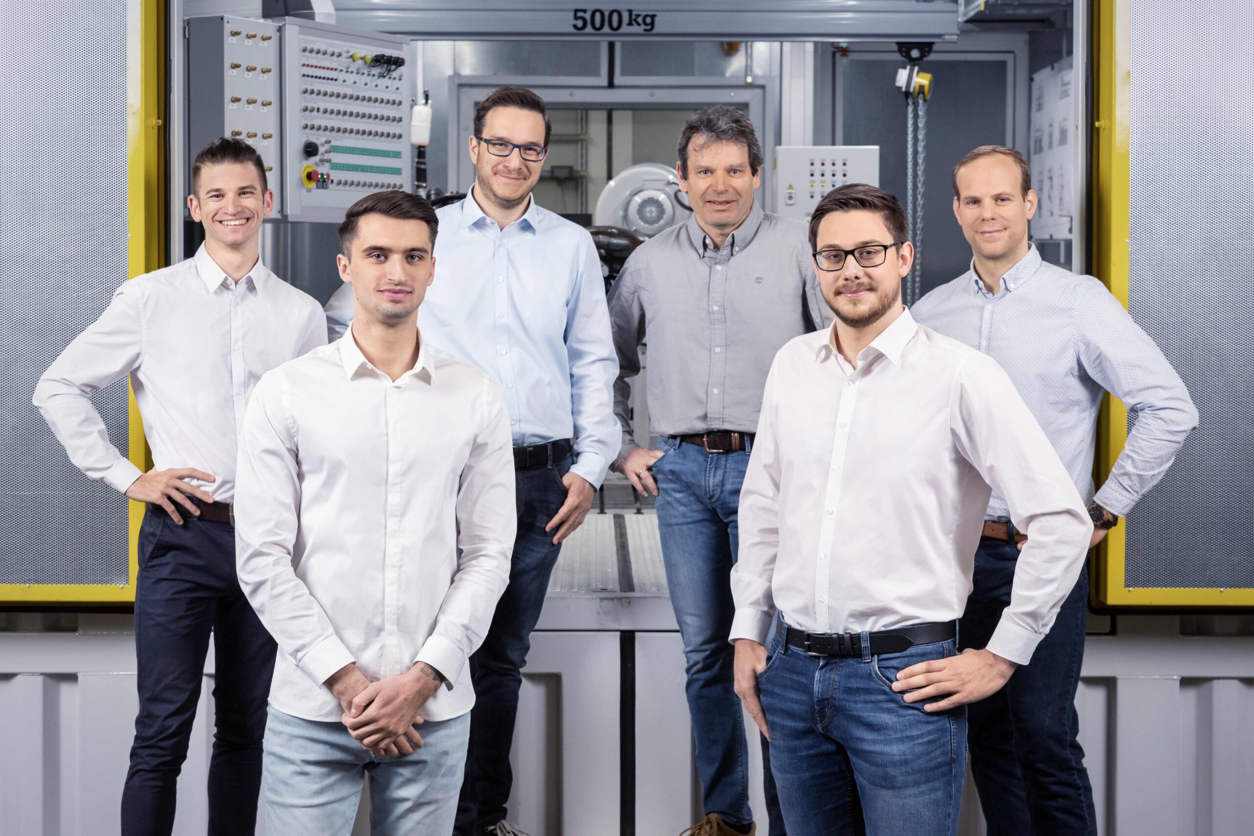 Portrait eines Teams bestehend aus sechs Personen vor einem Prüfstand stehend