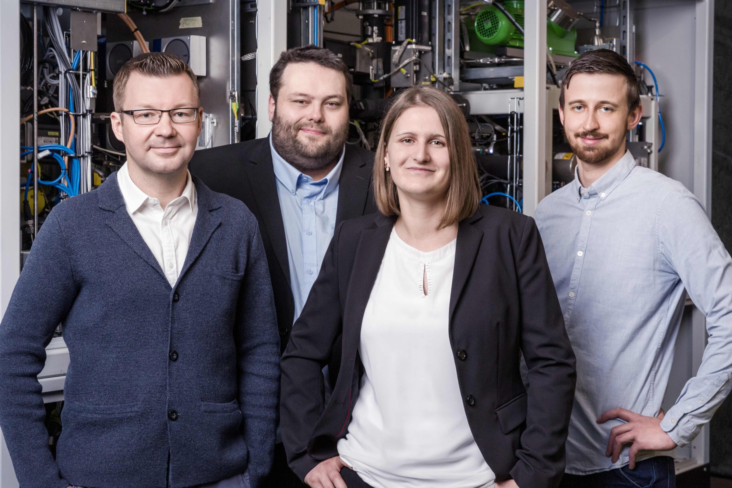 Portrait einer Gruppe von vier Personen vor einer Maschine