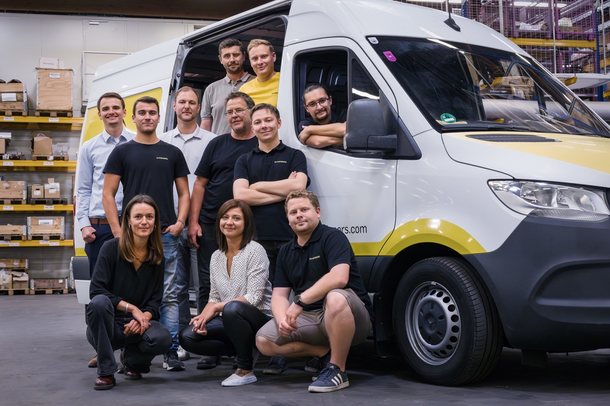 Ein Gruppenfoto von einem Team mit elf Personen, die vor einem Lieferwagen stehen